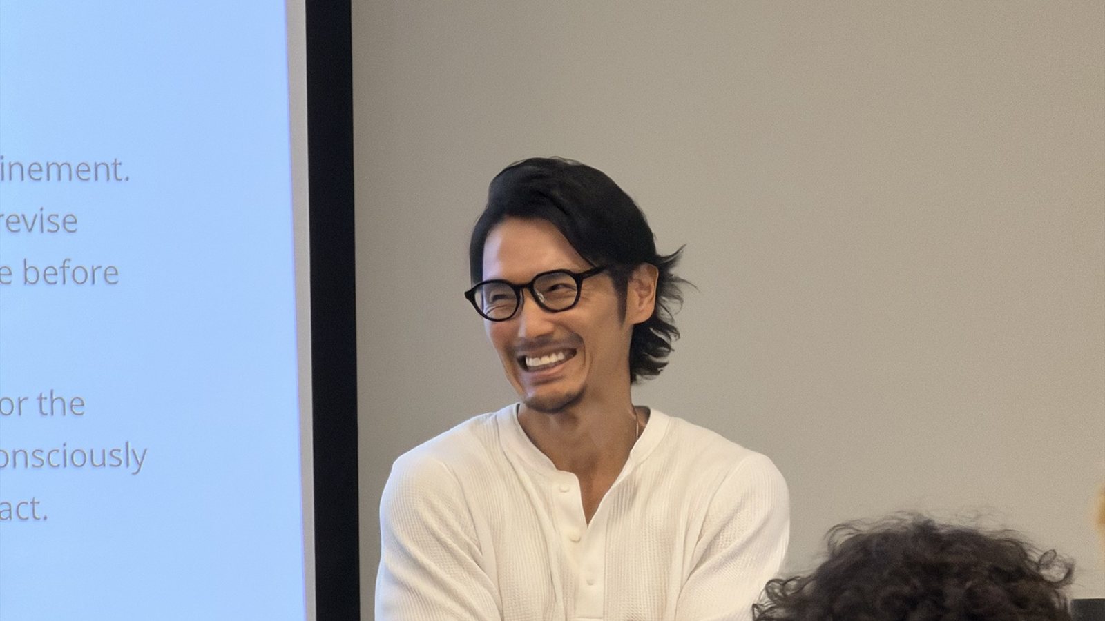 ハワイ大学の教室で、スライドの前に立ち笑顔で学生と話す藤井祐介