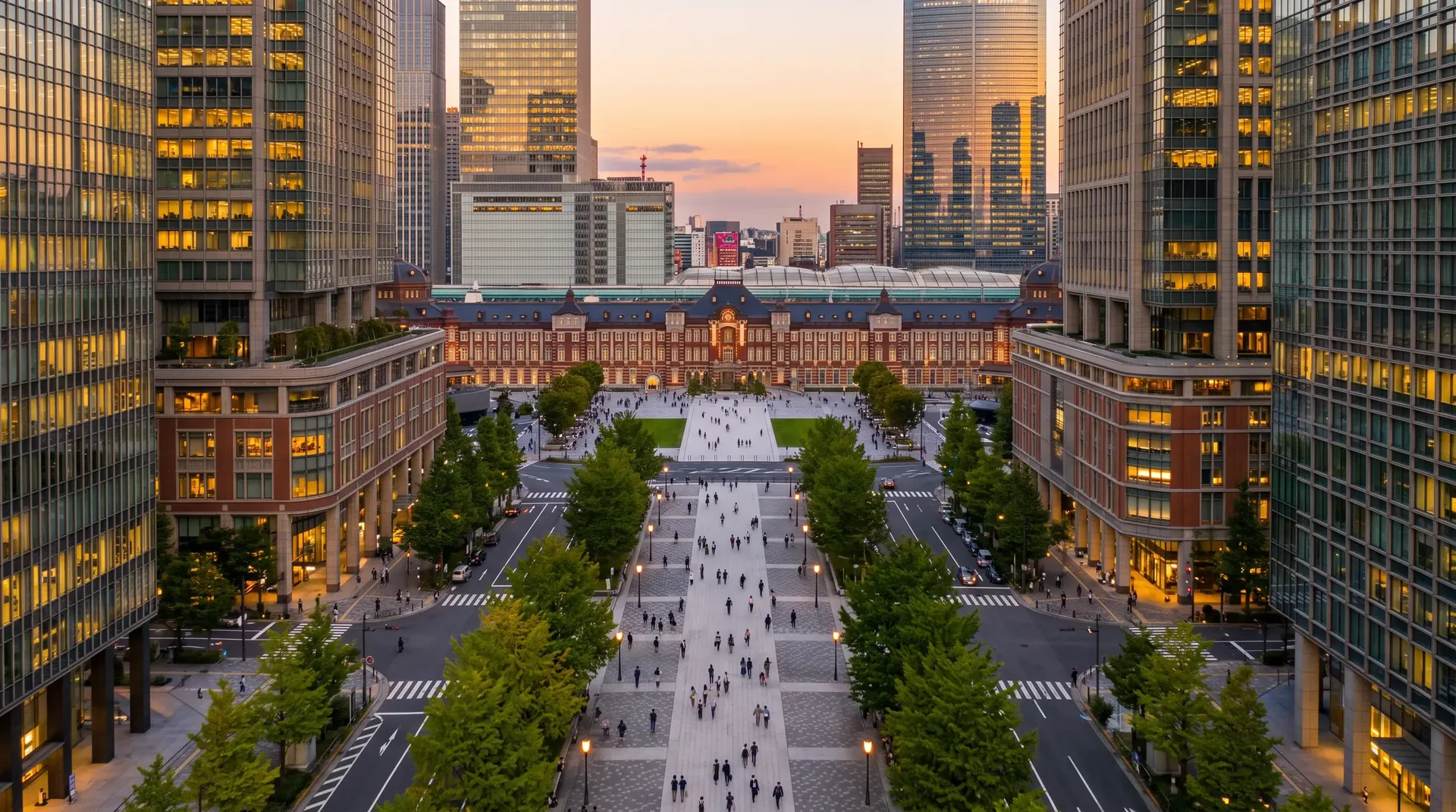 夕方のオフィス街。駅へ続く大通りを帰路につく人々と、灯りのともるビル